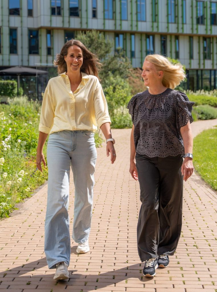Twee collega's van Antenna die buiten lopen, één lachend in de camera, de ander kijkend naar haar