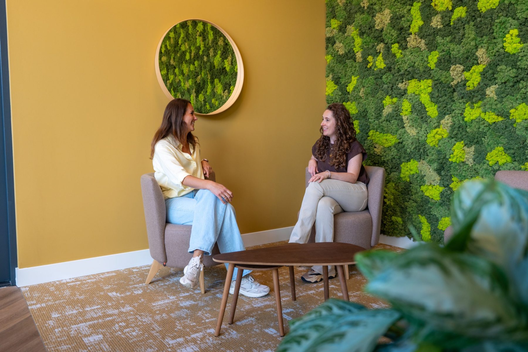 2 vrouwen zitten op een stoel in een ruimte en zijn in gesprek