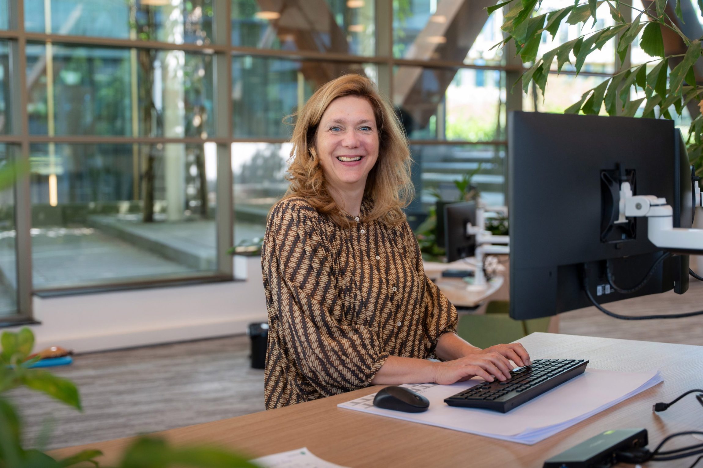 Collega kijkt lachend in de camera terwijl ze achter haar bureau staat