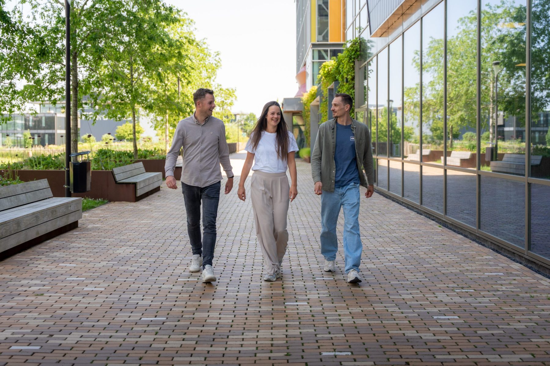 Drie lachende collega's van Antenna die samen buiten lopen en elkaar aankijken