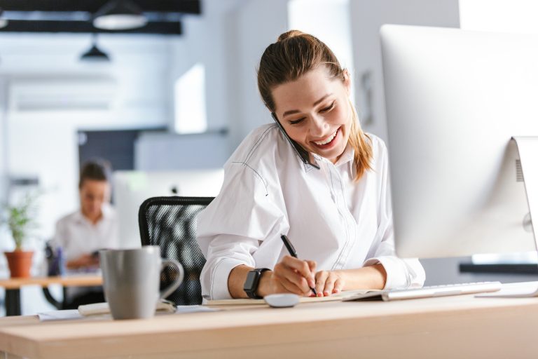 Vrouw zit achter bureau aan de telefoon en maak aantekeningen
