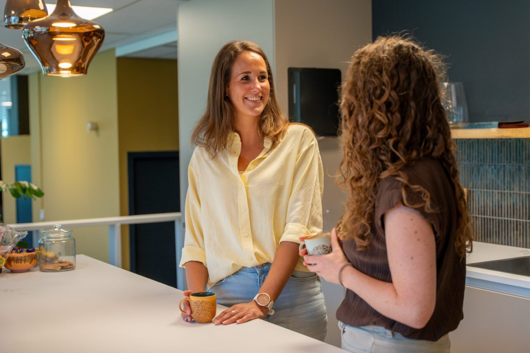 Twee collega's van Antenna die met elkaar praten in de keuken, de linker collega zichtbaar van voren, de ander van achteren.